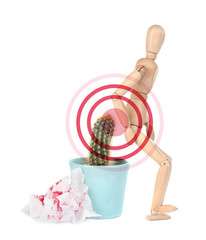 Hemorrhoid concept. Wooden human figure, cactus and sheets of toilet paper with blood on white...