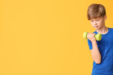 Sporty little boy with dumbbells on color background