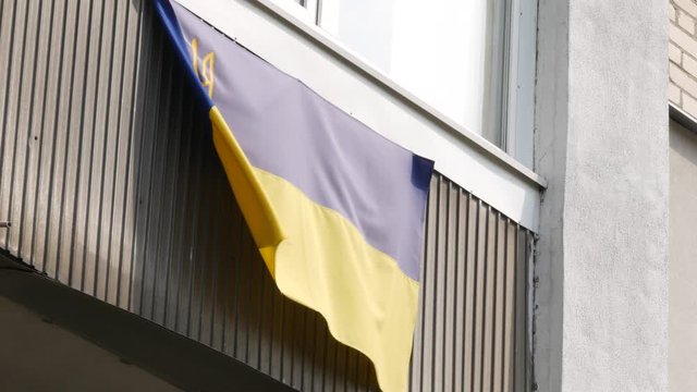 National flag of Ukraine is hung on balcony of residential building and flutters in wind. After events on Maidan in 2014 and war in east, patriotic citizens shows flags in windows and near houses