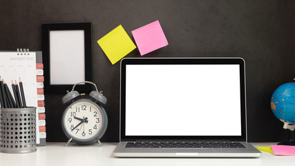 Laptop with blank screens and office equipment on the desk with black background wall