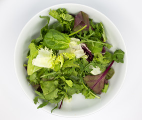 salad with different types of lettuce in a white bowl against a white background. lettuce, spinach, arugula and beet leaves.