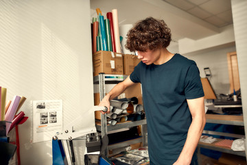 Printing arrangement. Portrait of man using machine for printing on baseball cap in workshop....