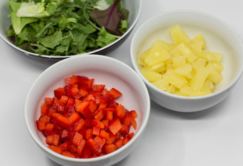chopped red pepper, pineapple and lettuce salad in white porcelain bowls on a white background. ingredients for salad