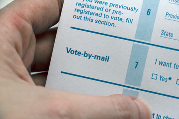 Hand holding Voter Registration form, closeup on Vote-by-mail