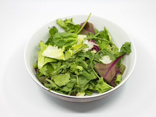 salad with different types of lettuce in a white bowl against a white background. lettuce, spinach, arugula and beet leaves.