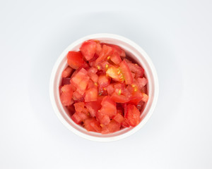 Chopped red tomato in a white porcelain bowl over white background