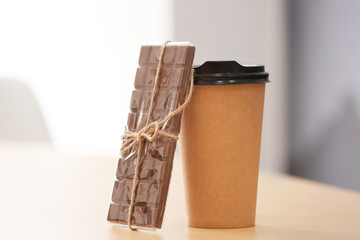 Takeaway cup with coffee and chocolate on table