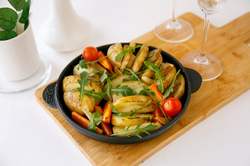 Baked young potatoes in a pan.  Large potato wedges with arugula leaves and cherry tomatoes.