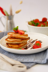 Breakfast: lush vanilla pancakes garnished with strawberries and chocolate sauce.  Pancakes with strawberries on a white plate on a blue napkin