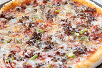 Homemade pizza fresh from the oven and unsliced.  Topped with pepperoni, cheese, peppers, onions, and beef.