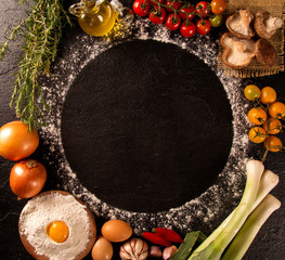Various vegetables at black concrete background with copyspace on round pizza desk. Set of fresh vegetables. Egg, tomatoes, pepper, lettuce, onion, garlic, onion. Pizza ingredients.