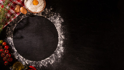 Various vegetables at black concrete background with copyspace on round pizza desk. Set of fresh vegetables. Egg, tomatoes, pepper, lettuce, onion, garlic, onion. Pizza ingredients.