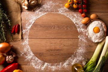 Various vegetables at wooden rustic background with copyspace on round pizza desk. Set of fresh vegetables. Egg, tomatoes, pepper, lettuce, onion, garlic, onion. Pizza ingredients.