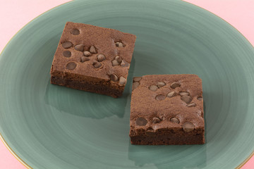Two chocolate chip brownie squares on blue plate on pink background