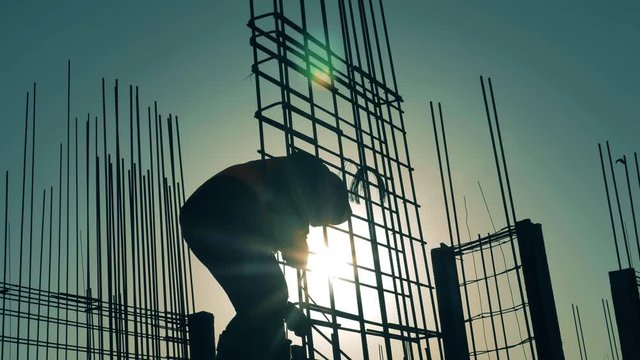 Construction worker works with armature on sunset background.