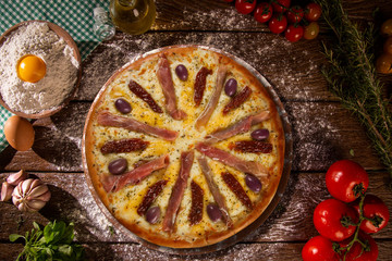 Tasty prosciutto pizza and cooking ingredients tomatoes basil on wood background. Top view prosciutto pizza