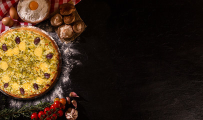 Tasty leek and mushrooms pizza and cooking ingredients tomatoes basil on black concrete background. Top view of leek pizza