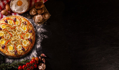 Tasty portuguese pizza and cooking ingredients tomatoes basil on black concrete background. Top view.
