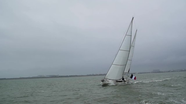 Sailing yacht heeling and cutting through the water with waves splashing in slow motion. Filmed in France, La Rochelle.