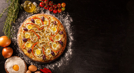 Tasty portuguese pizza and cooking ingredients tomatoes basil on black concrete background. Top view.