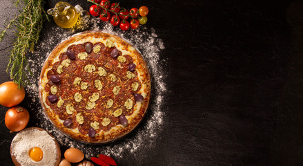 Tasty pepperoni and mushrooms pizza and cooking ingredients tomatoes basil on black concrete background. Top view of pepperoni pizza