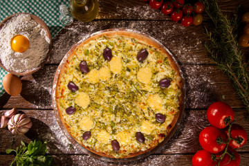 Tasty leek and mushrooms pizza and cooking ingredients tomatoes basil on wood background. Top view of leek pizza