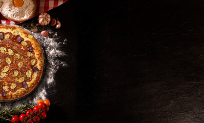 Tasty pepperoni and mushrooms pizza and cooking ingredients tomatoes basil on black concrete background. Top view of pepperoni pizza