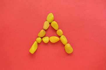 Letter A made of old Yellow pebbles on a red background