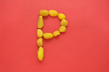 Letter P made of old Yellow pebbles on a red background