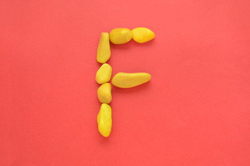 Letter F made of old Yellow pebbles on a red background