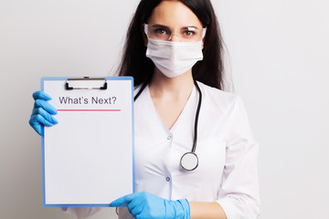 Doctor in a gloves, mask and glasses holds sheet with text what's next.