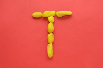 Letter T made of old Yellow pebbles on a red background