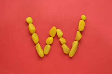 Letter W made of old Yellow pebbles on a red background