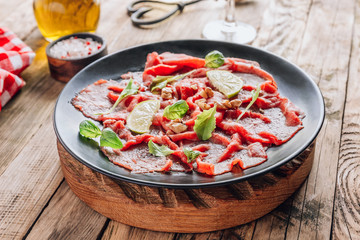 Black plate with carpaccio of beef with baby arugula, lime and white wine on rustic wooden background.