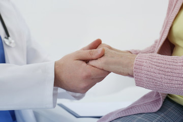 Doctor and senior patient holding hands in hospital, closeup