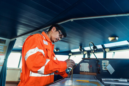 Filipino deck Officer on bridge of vessel or ship wearing coverall during navigaton watch at sea . He is plotting position on chart