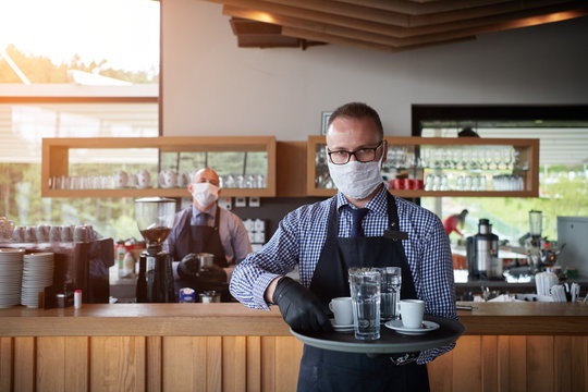 waiter in a medical protective mask serves  the coffee in restaurant