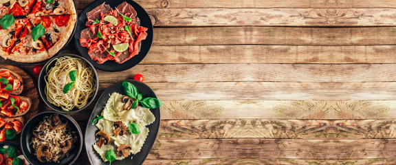Fototapeta na wymiar Table of italian meals on plates Pizza, pasta, ravioli, carpaccio, mushroom risotto, caprese salad and tomato bruschetta on rustic wooden background.