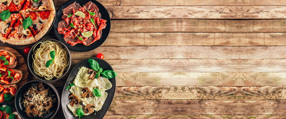 Table of italian meals on plates Pizza, pasta, ravioli, carpaccio, mushroom risotto, caprese salad and tomato bruschetta on rustic wooden background.