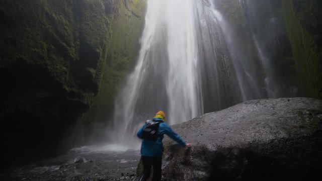 A man hikes up onto a giant boulder near a hidden waterfall in Iceland