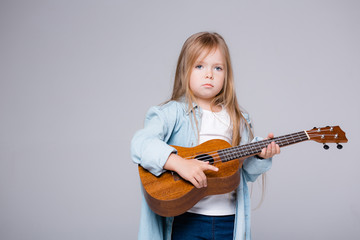 Girl child plays on ukuleles on a gray background. Children's creativity