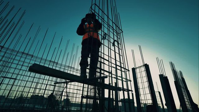 Male builder knits rods on reinforcement. Construction worker silhouette.