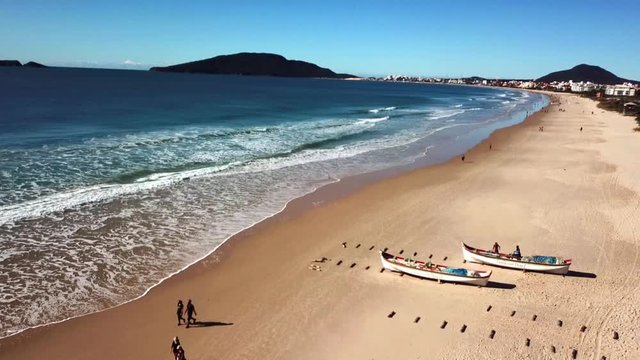 Zoom out - Aerial view of people practicing physical exercises on the beach during mullet fishing in Brazil. Wooden boats anchored on the shore waiting for fish.