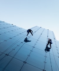 Low angle shot of two persons rappelling at the side of a tall building - obrazy, fototapety, plakaty