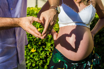 A couple making a heart shape on the pregnant belly with their hands. Concept of pregnancy, expecting a baby, love, care