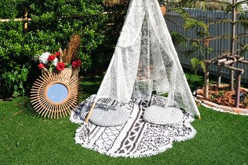 Outdoor white lace tent with round seat cushions, rattan mirror, red roses and plants