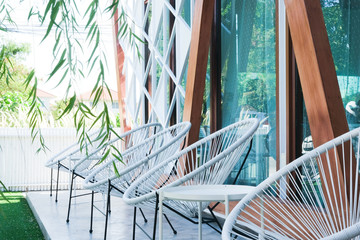 5 white rattan chair with the small white table against the glass and wood wall