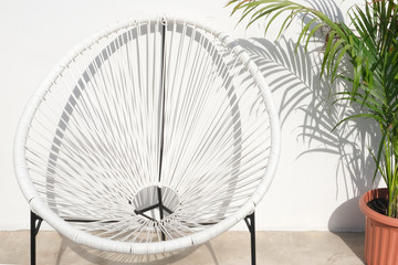 white rattan chair and the plant in brown pot against the white wall.