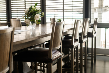 Empty wooden chairs with leather padding are set around tables in restaurant