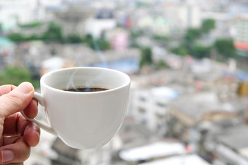 Hand of a man holding a hot coffee cup with smoke at the new morning on a modern city background